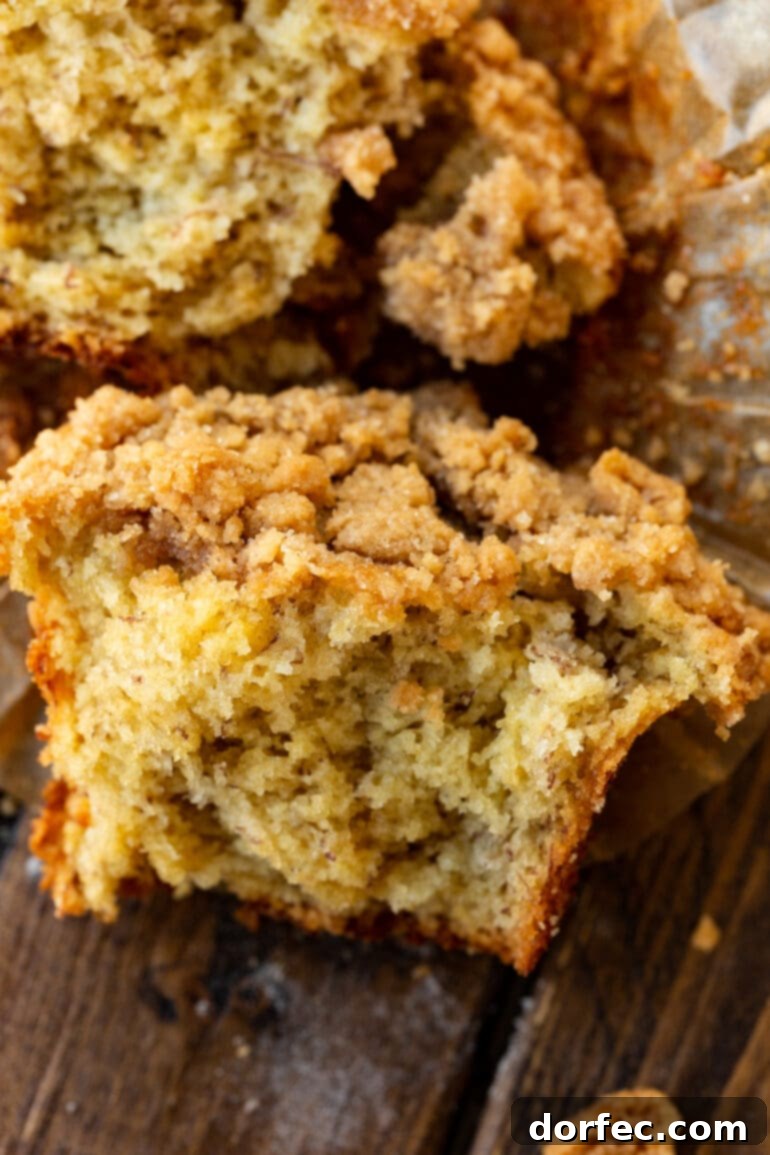 Ultimate Streusel Banana Bread Muffins 5 A tender, moist bakery-style banana crumb muffin, broken open to reveal its fluffy texture and generous crumb topping. Focus is on the rich banana flavor and inviting texture.