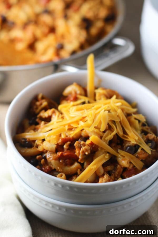 Delicious Healthy One-Pot Chili Mac Serving Close-up of a bowl of homemade healthy chili mac, topped with shredded cheese and fresh herbs