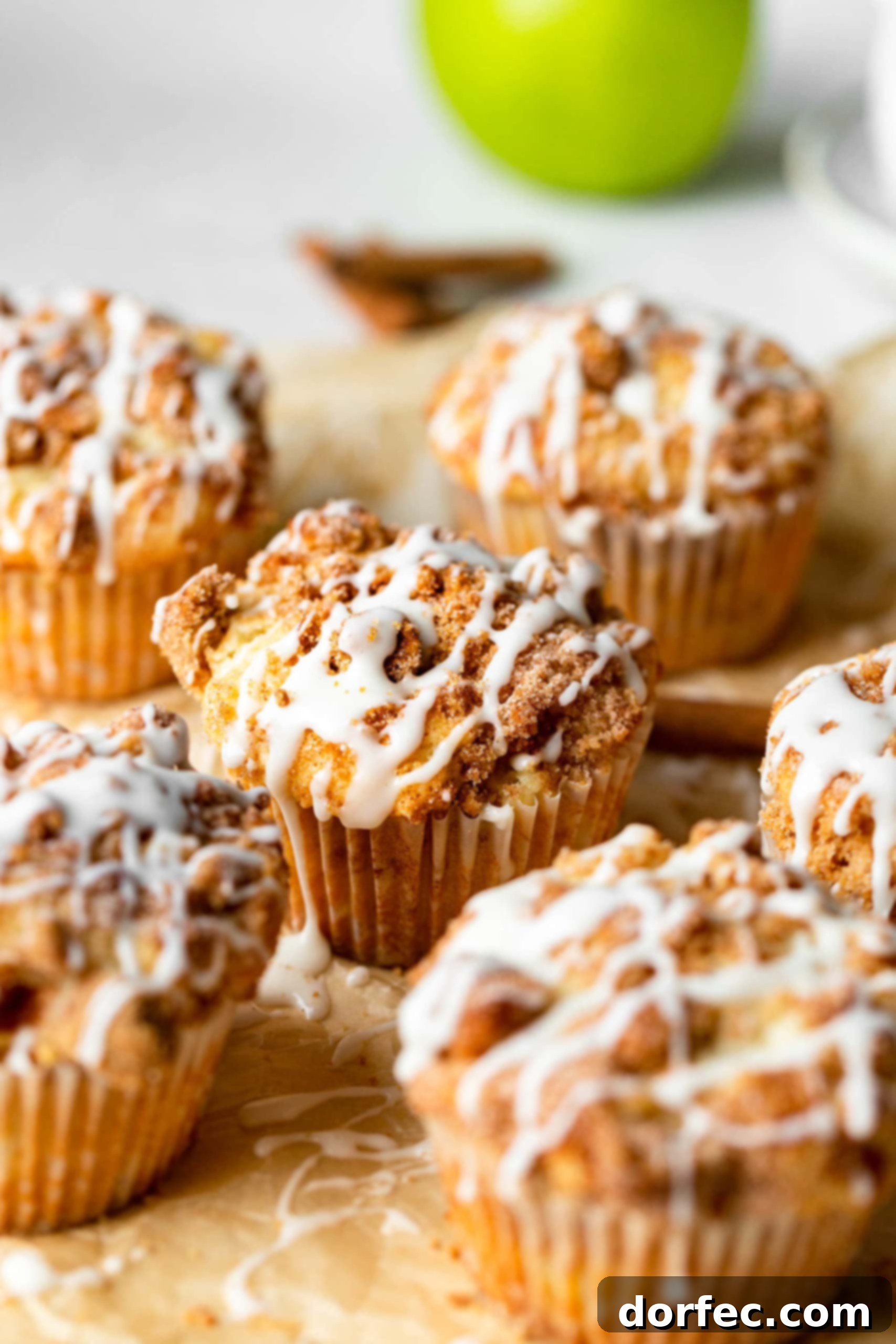 Spiced Apple Coffee Cake Muffins 2 A collection of freshly baked apple coffee cake muffins, featuring generous streusel and a light icing, arranged on natural parchment paper, highlighting their bakery-style appearance.