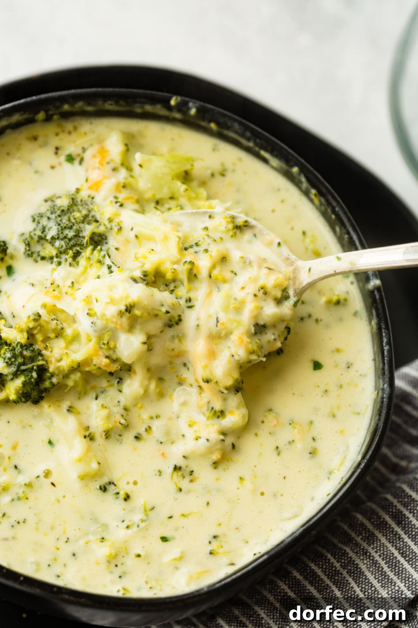 A captivating overhead shot of a black bowl showcasing a hearty slow cooker broccoli cheese soup, generously topped with an inviting layer of extra shredded cheese.