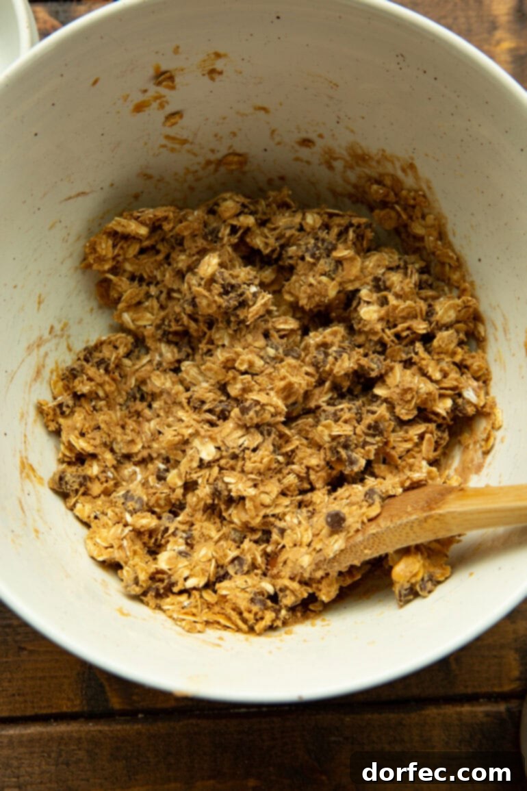 A close-up shot of the oatmeal energy bites mixture being thoroughly combined in a large white bowl with a wooden spoon, showing the rich texture and chocolate chips.