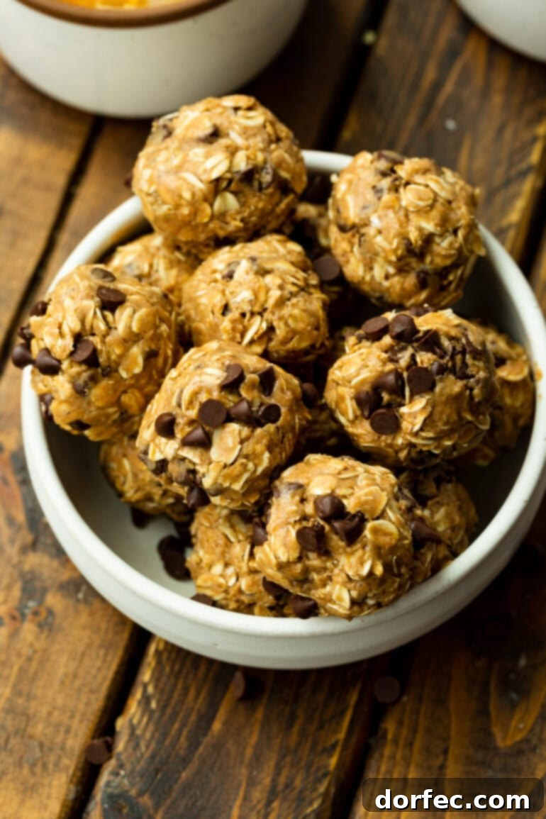 A large, rustic white bowl elegantly filled with dozens of perfectly rolled oatmeal protein balls, scattered with visible chocolate chips, promising a wholesome and satisfying snack.