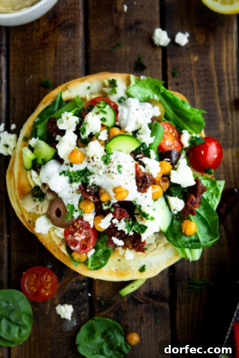 A photo taken over the top of a Greek tostada topped with cucumber, tomatoes, chickpeas, olives, feta, and tzatziki sauce, highlighting the fresh ingredients.