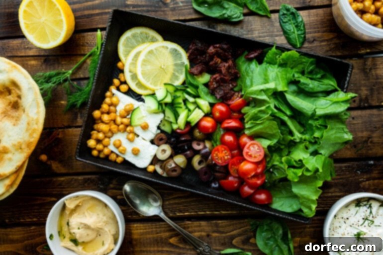 A photo of a tray full of all the Greek-inspired toppings for Greek tostadas including tomatoes, lettuce, olives, chickpeas, lemons, cucumbers, feta, and sun-dried tomatoes, showcasing a vibrant spread.