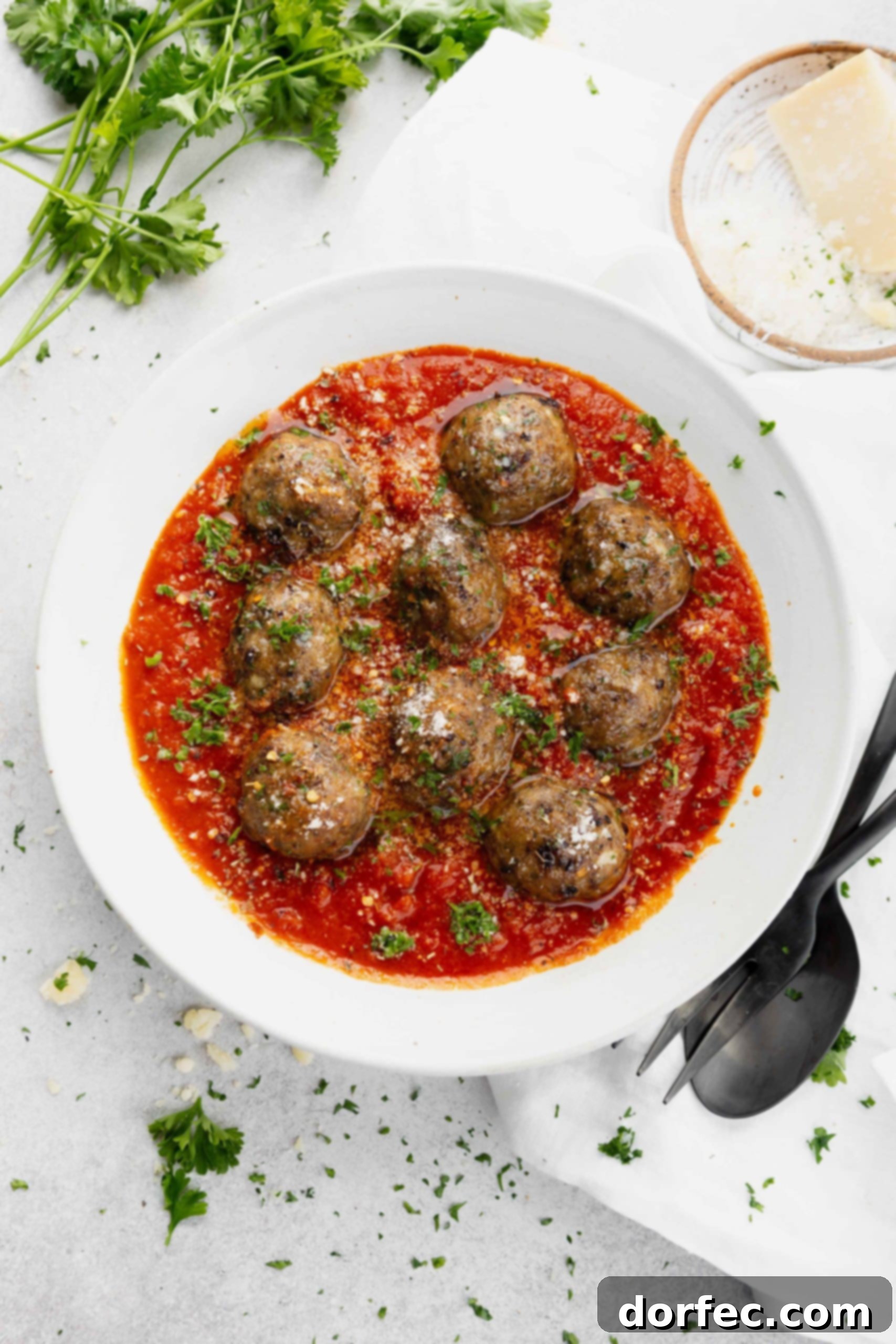 A delicious serving of spaghetti and meatballs, adorned with fresh parsley, served alongside a fork and spoon, ready to be enjoyed.