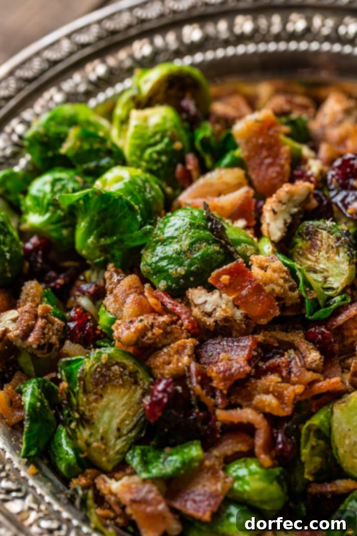 A vintage, silver bowl overflowing with bright green halved Brussels sprouts, pan-roasted to golden brown perfection, tossed with vibrant red craisins, crispy bacon bits, and crunchy candied pecans. The dish is beautifully presented, hinting at a delightful culinary experience.