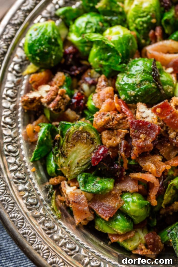 A vibrant display of pan-roasted Brussels sprouts in a silver bowl, garnished with candied pecans, crispy bacon, and red craisins, ready to be served as a gourmet side dish.