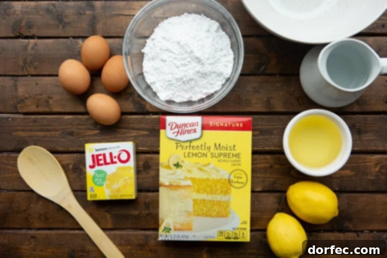 A flat lay photo of all the essential ingredients for a Lemon Jello Cake, including a box of lemon cake mix, a packet of lemon Jell-O, fresh lemons, eggs, oil, and powdered sugar.