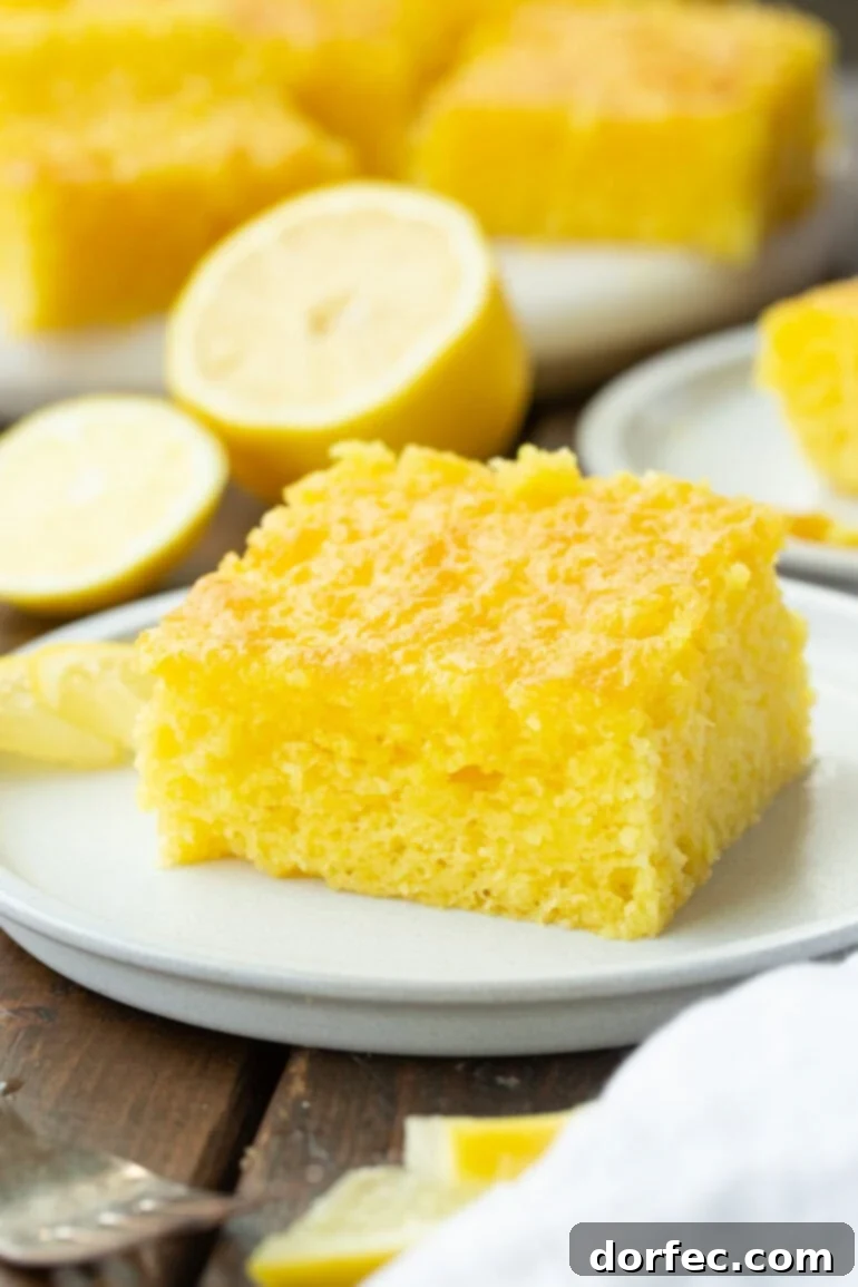 A pristine slice of moist Lemon Jello Cake sitting on a small white dessert plate, ready to be enjoyed.