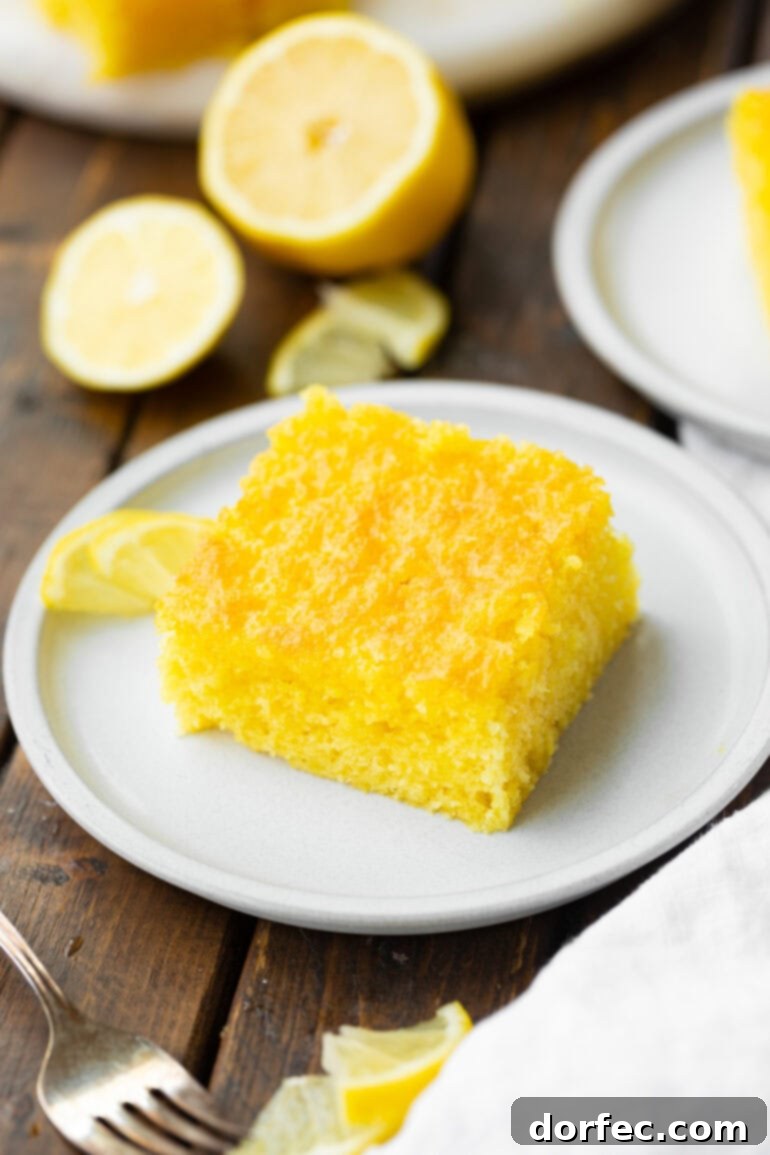 A vibrant slice of bright yellow Lemon Jello Cake presented on a small white dessert plate.