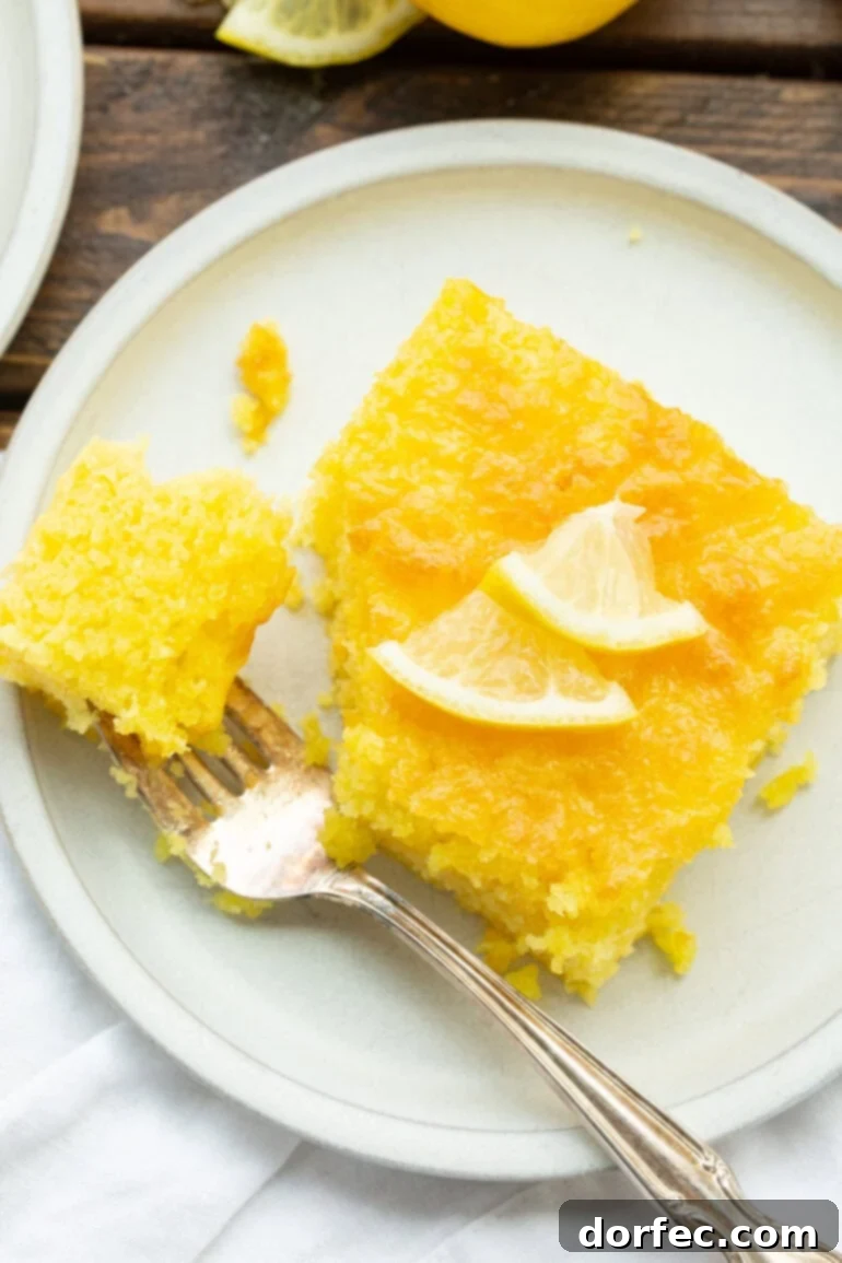 A close-up shot of a piece of lemon cake with a silver fork removing a bite from its corner, highlighting its soft texture.