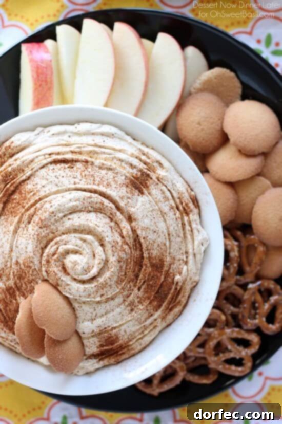 Pumpkin Dip artfully presented in a white serving bowl, positioned on a sleek black plate alongside an array of complementary dippers including pretzels, crispy wafers, and vibrant red apple slices, creating a visually appealing autumn dessert display.