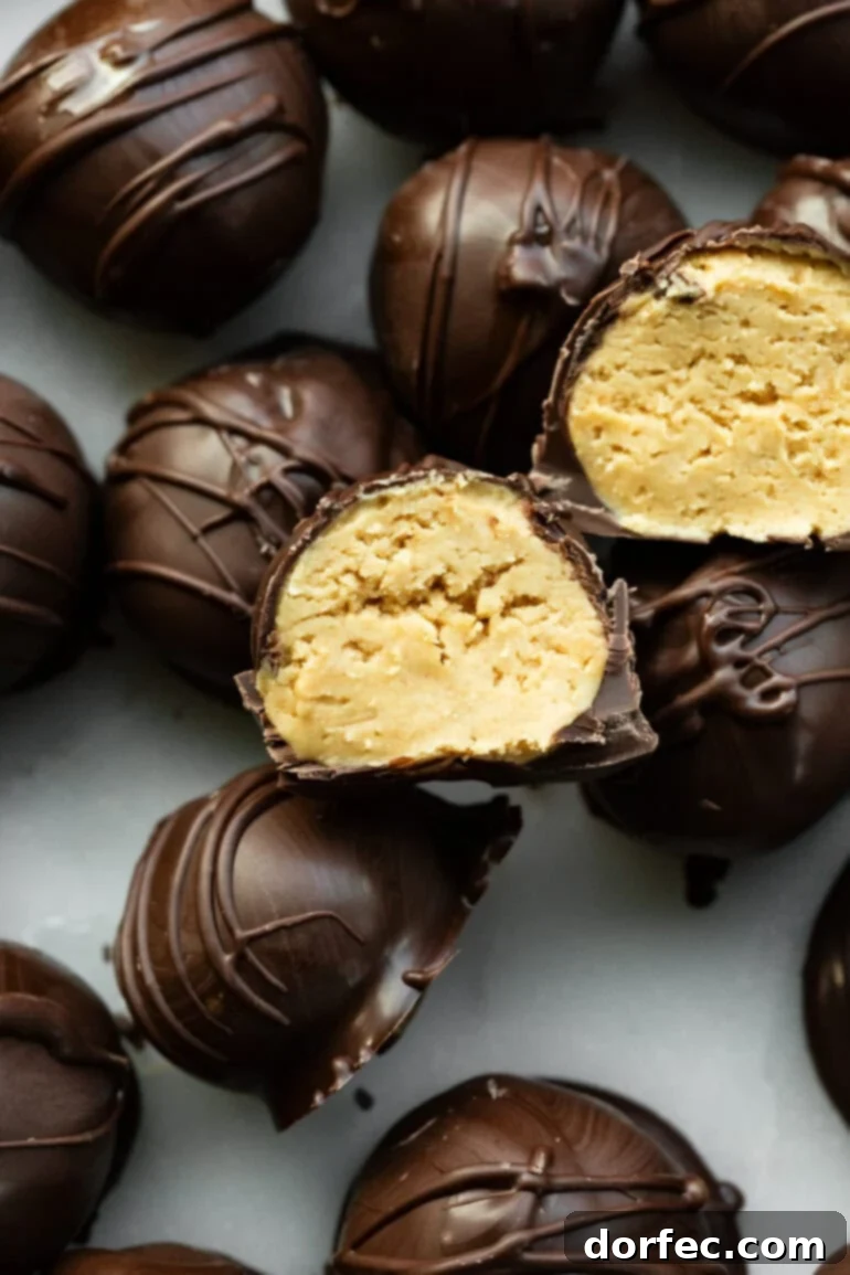 A photo of several dark chocolate-covered peanut butter balls, with two sliced in half revealing the creamy peanut butter filling inside.