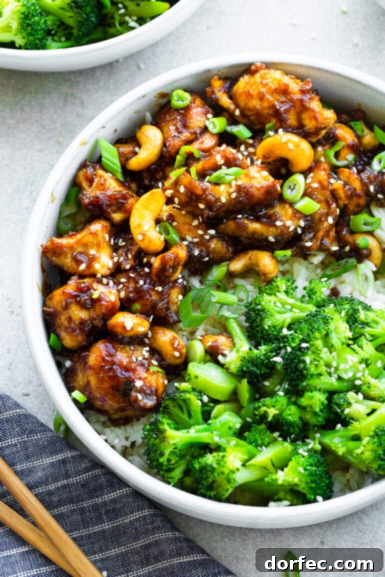 A vibrant photo of saucy cashew chicken bites mingled with cashews, served with a side of steamed green broccoli florets.