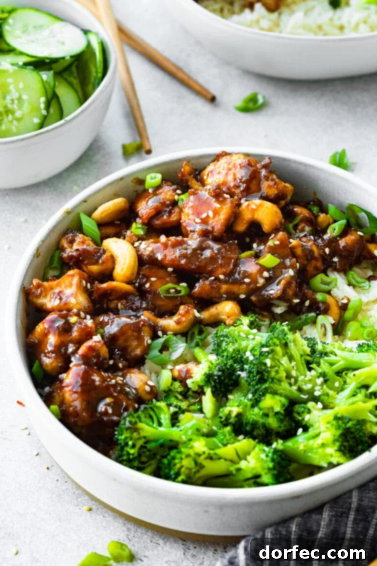 A bowl of golden cooked chicken chunks coated in a sweet, sticky sauce and mixed with roasted nuts, served with a side of bright green steamed broccoli.