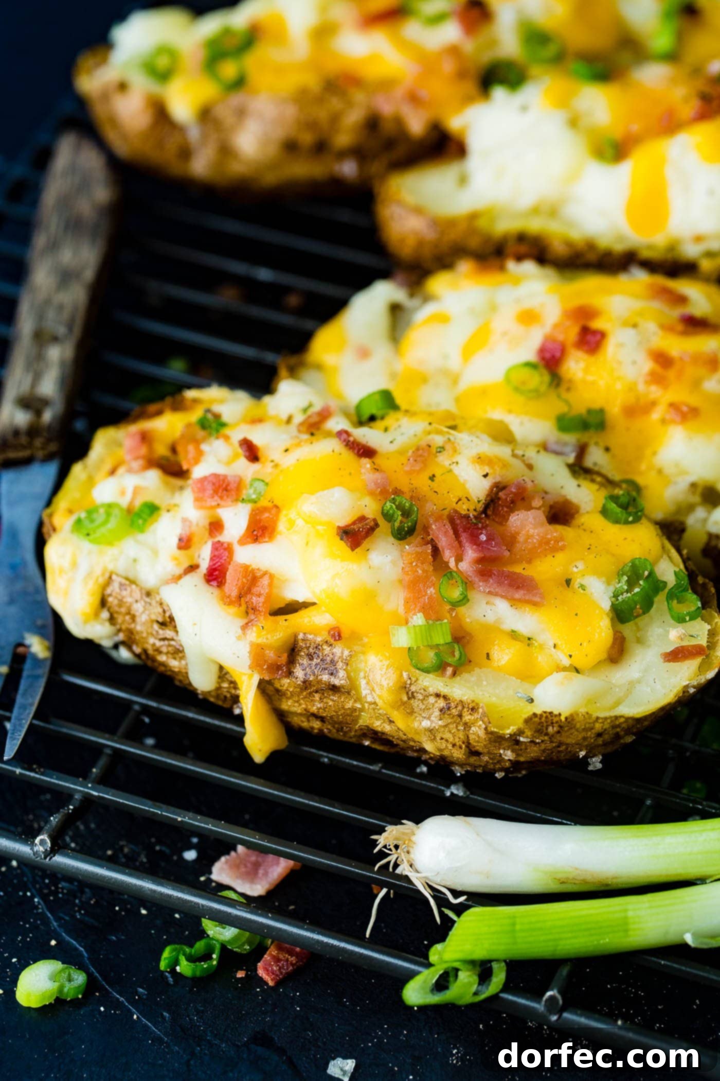A cooling rack displaying a perfect lineup of loaded twice baked potatoes, generously topped with melted cheese and crispy bacon