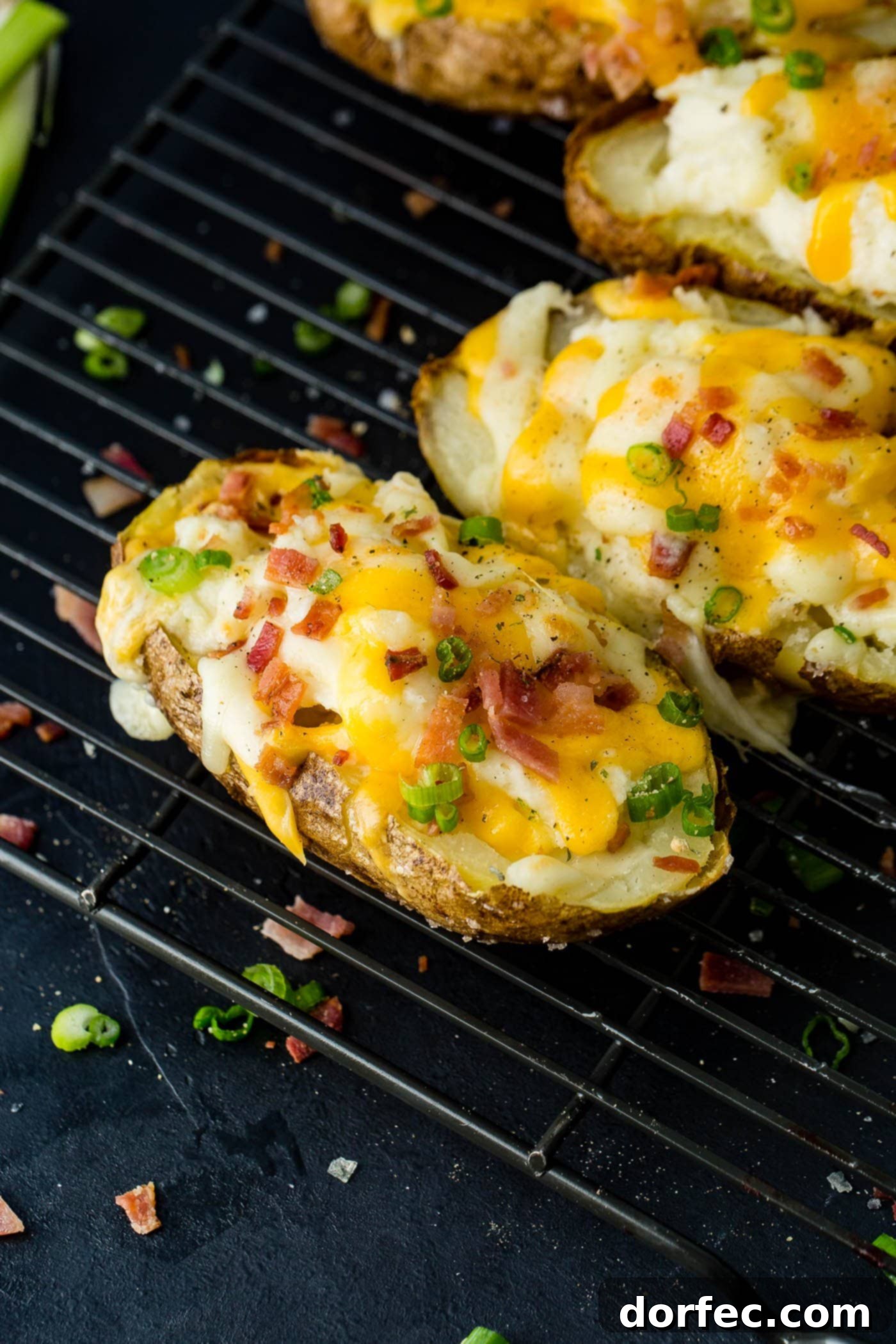 A cooling rack showcasing a beautiful row of loaded twice baked potatoes, each generously topped with melted cheese and crispy bacon for a savory side