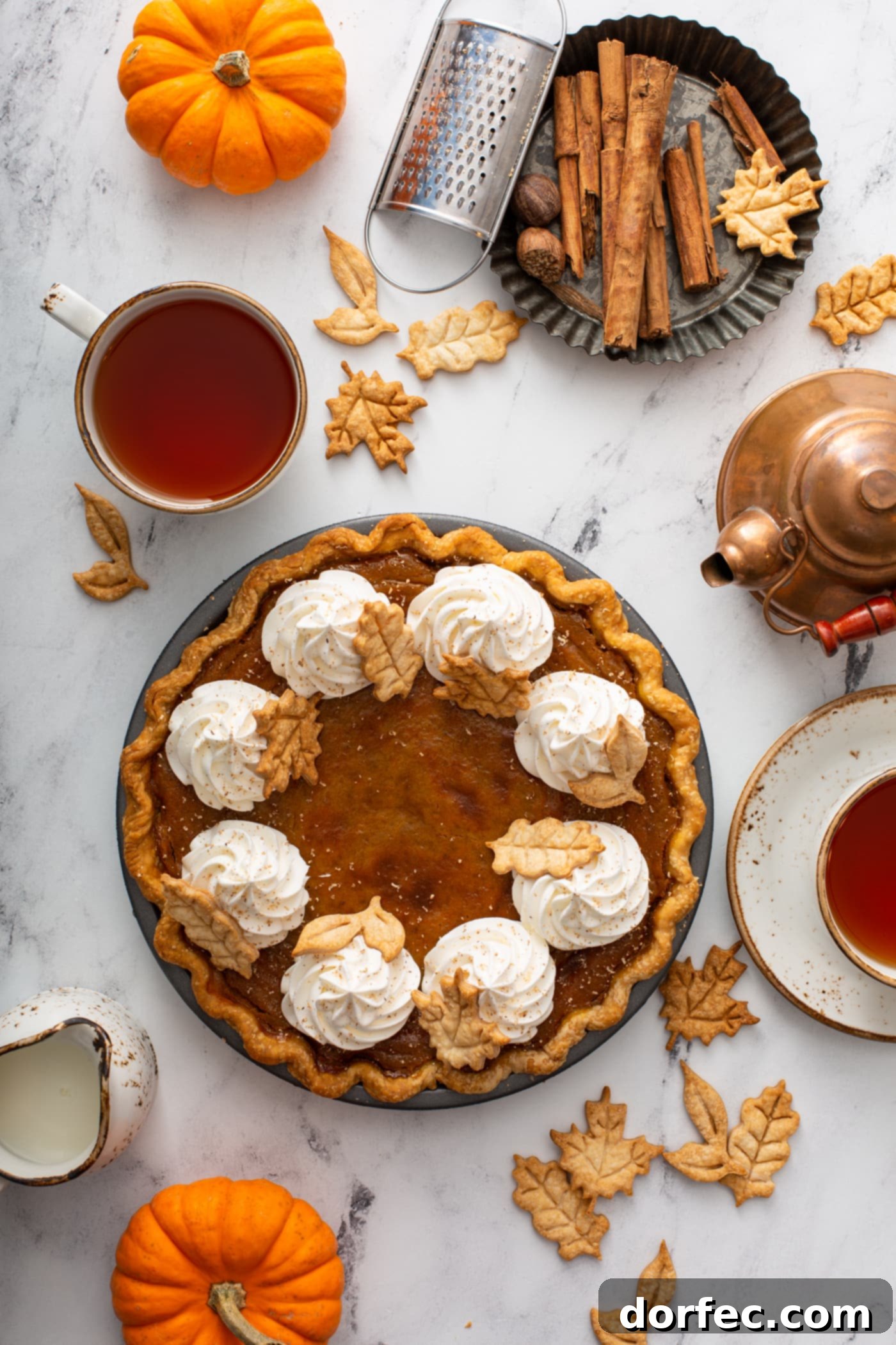 A golden-brown homemade pumpkin pie sits on a cooling rack, beautifully garnished with elegant piped whipped cream and delicate pie crust leaves, showcasing a perfect autumnal dessert.