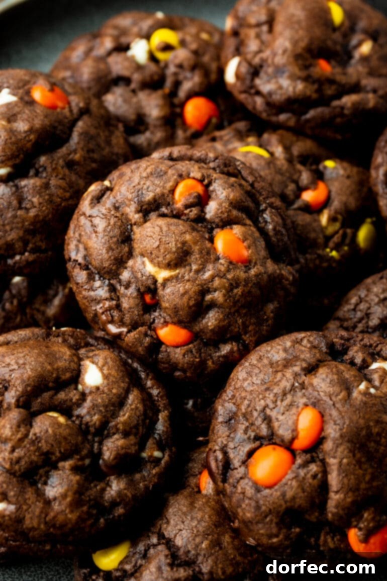 A pile of several thick and chewy Reese's Triple Chocolate Cookies resting on a wire cooling rack, highlighting their generous size and tempting texture.