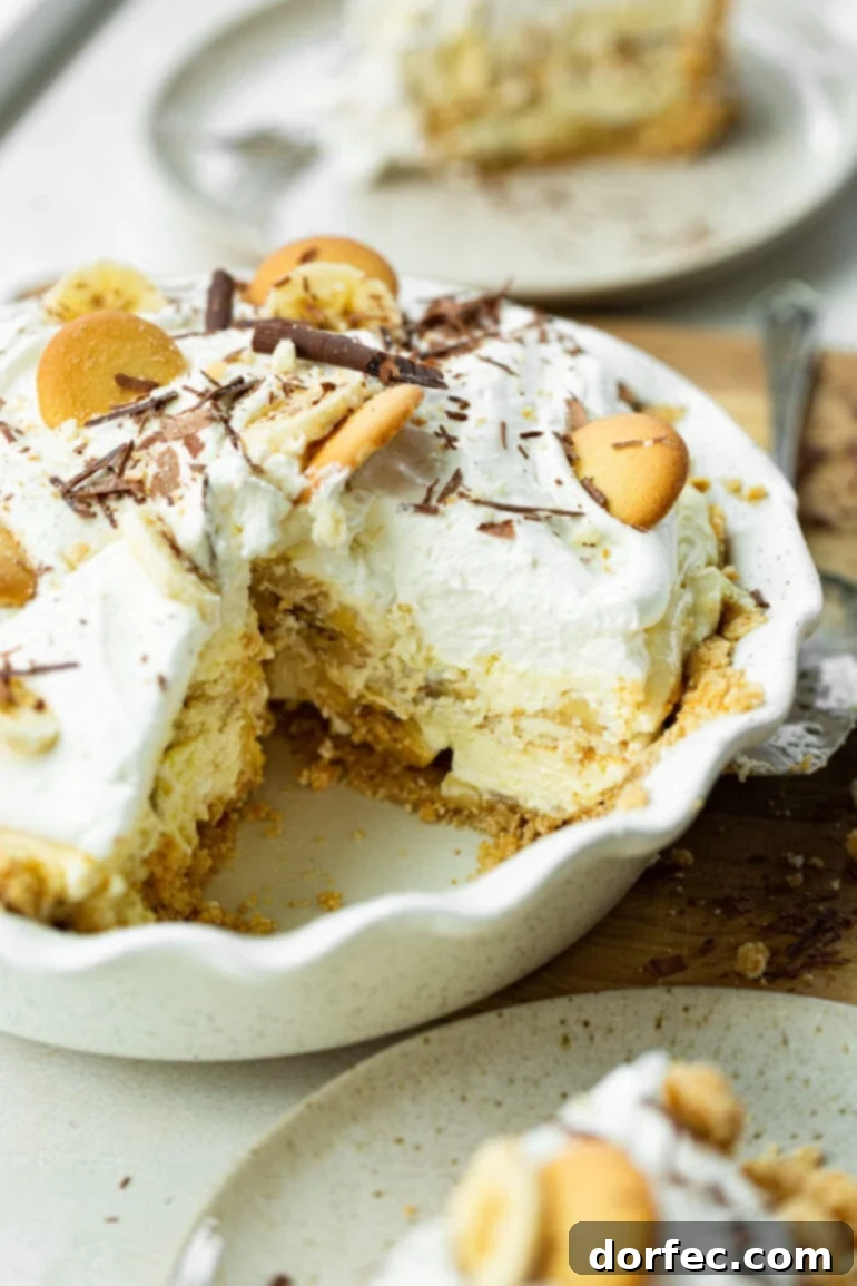 A photo of a thick, creamy banana cream pudding pie in a white baking dish with a piece removed so you can see the inside.