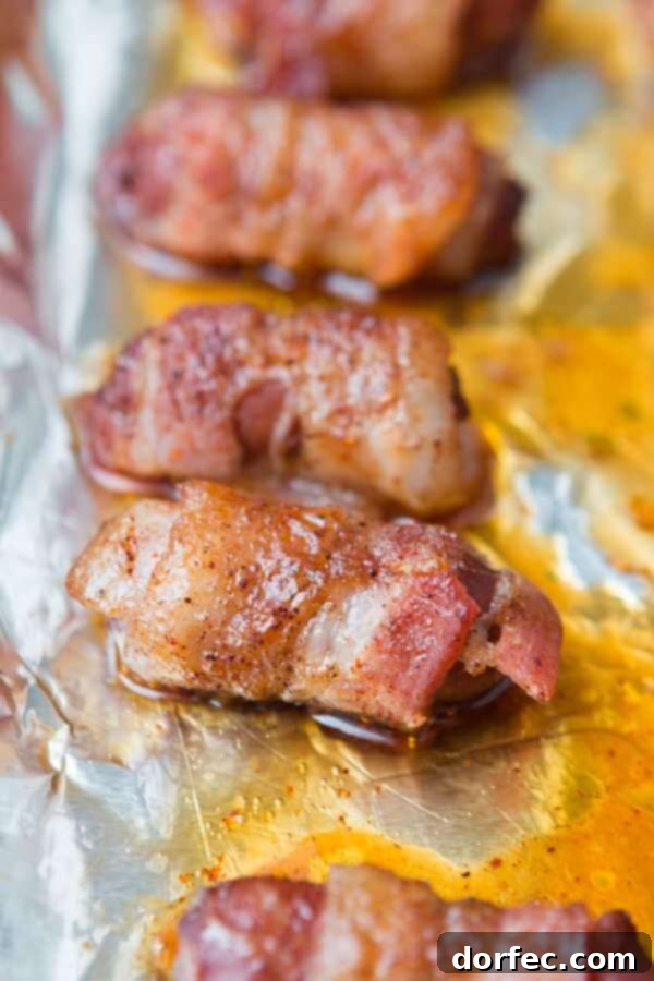 Simple and Quick Bacon-Wrapped Little Smokies Appetizer Freshly baked bacon-wrapped little smokies on a foil-lined baking tray, showing the crispy bacon and melted brown sugar glaze.