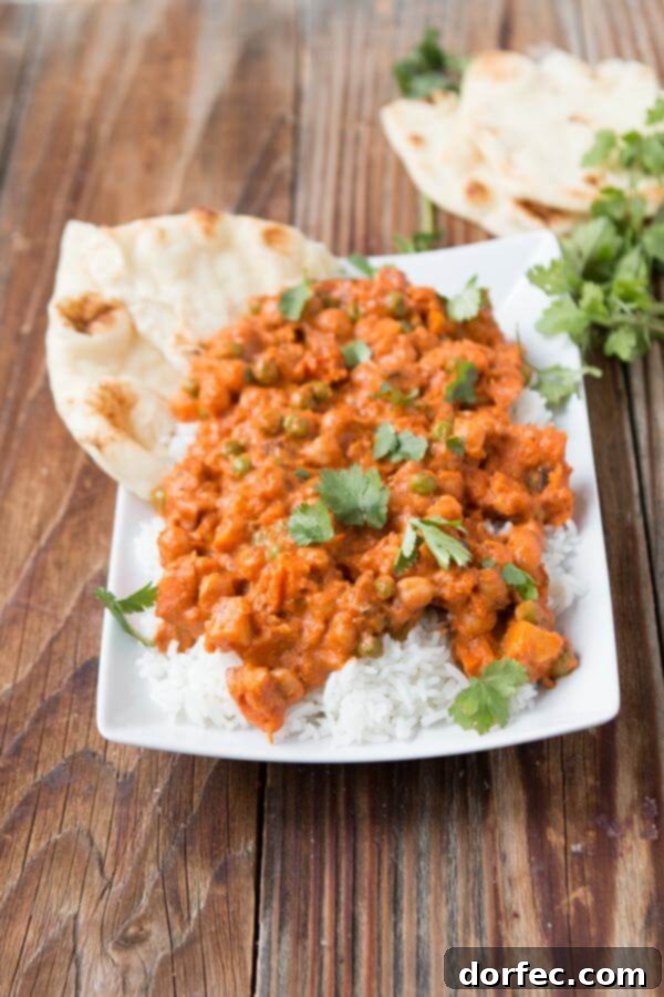 A vibrant bowl of homemade vegetarian Bombay House Tikka Masala, garnished with fresh cilantro, served alongside fluffy naan bread and steaming white rice.