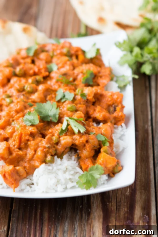Ingredients for vegetarian Tikka Masala laid out on a wooden cutting board, including fresh sweet potatoes, chickpeas, and a selection of aromatic spices.
