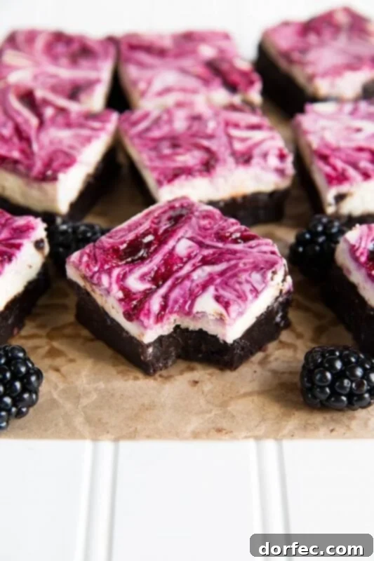 A stunning close-up of several square fudgy brownies topped with a creamy cheesecake layer beautifully swirled with vibrant blackberry puree, with fresh whole blackberries scattered around the dessert, highlighting its richness and fruitiness.