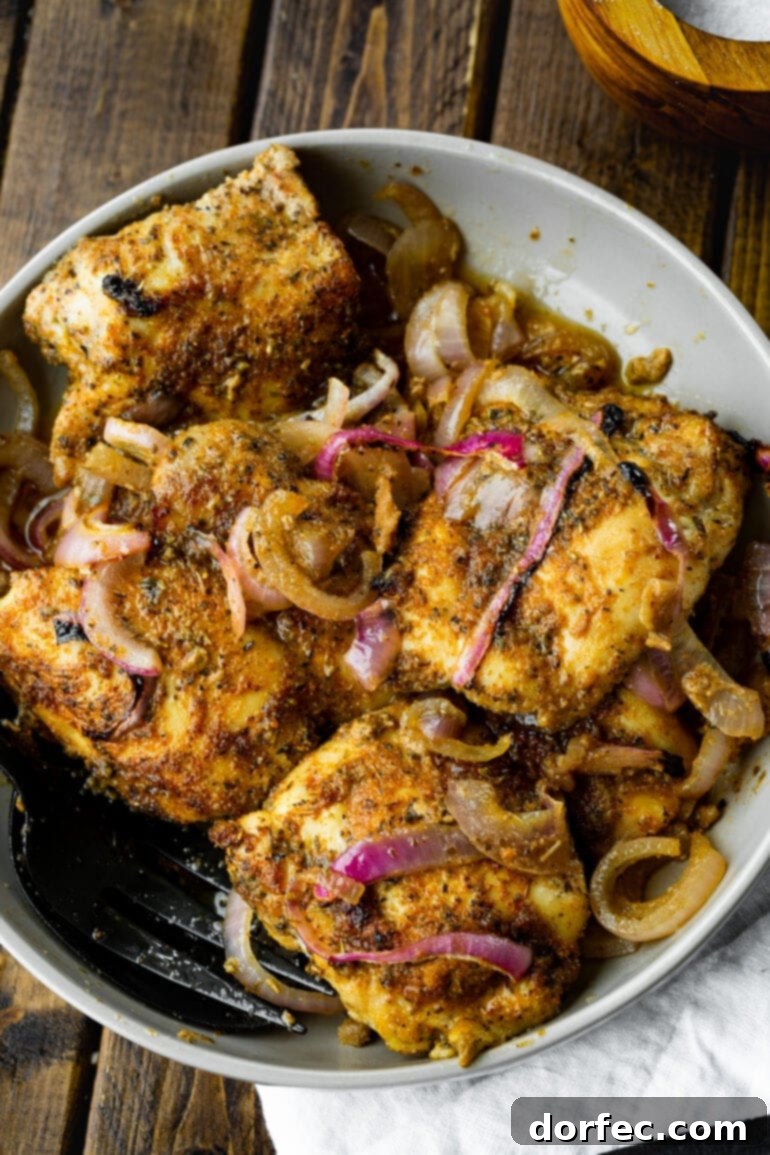 A photo of several golden baked chicken thighs mixed with slices of red onion, ready to be served.