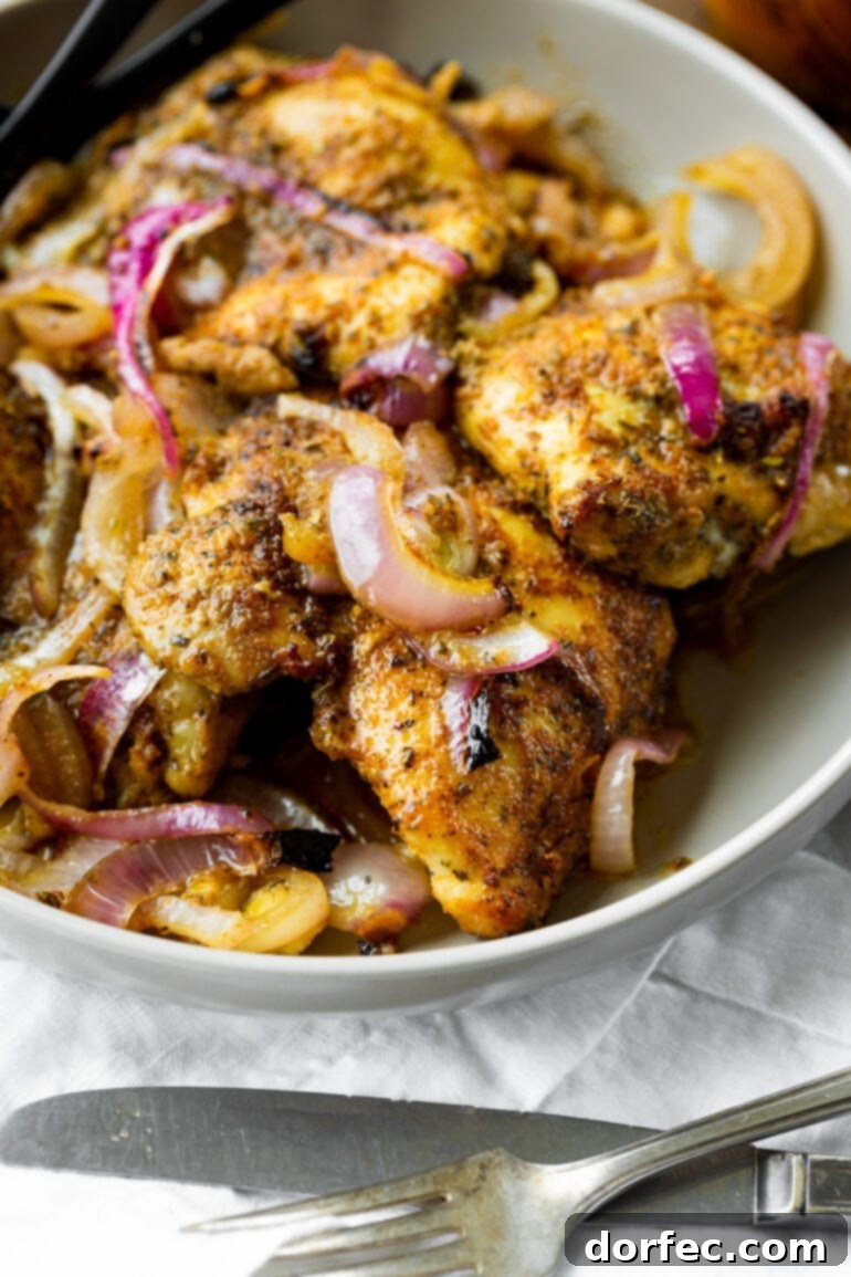 A photo of a large white serving bowl full of several golden baked chicken thighs mixed with cooked red onions.
