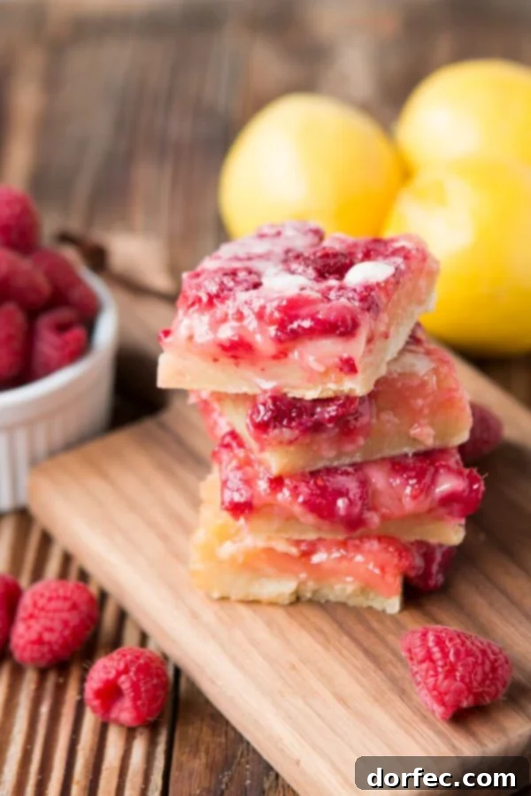 Several vibrant Raspberry Lemon Bars stacked on a wooden cutting board, with fresh whole raspberries scattered around them, highlighting their appealing texture and color.