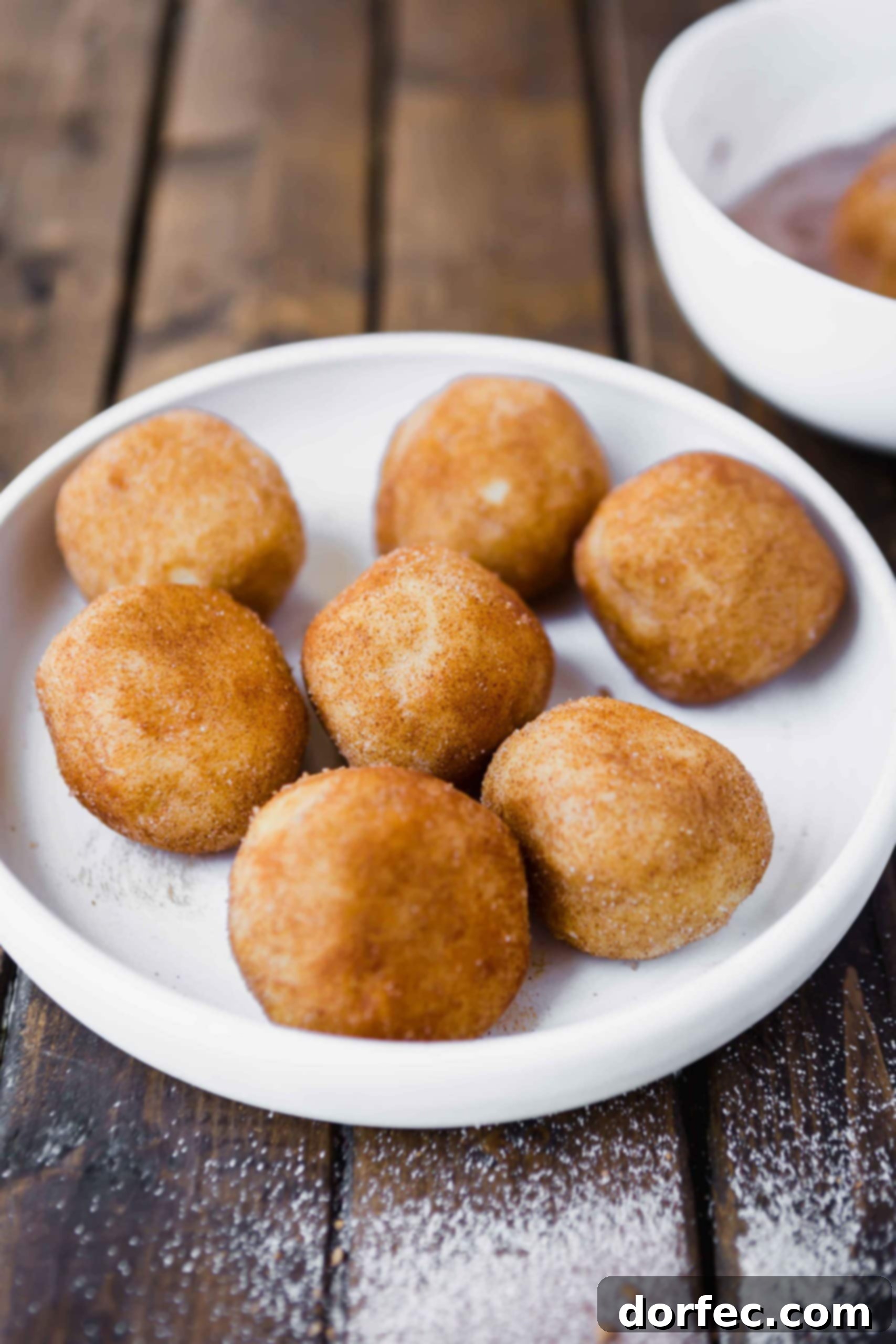 A photo of seven balls of snickerdoodle cookie dough that have been rolled in cinnamon sugar, neatly arranged on a white plate, ready for the oven.