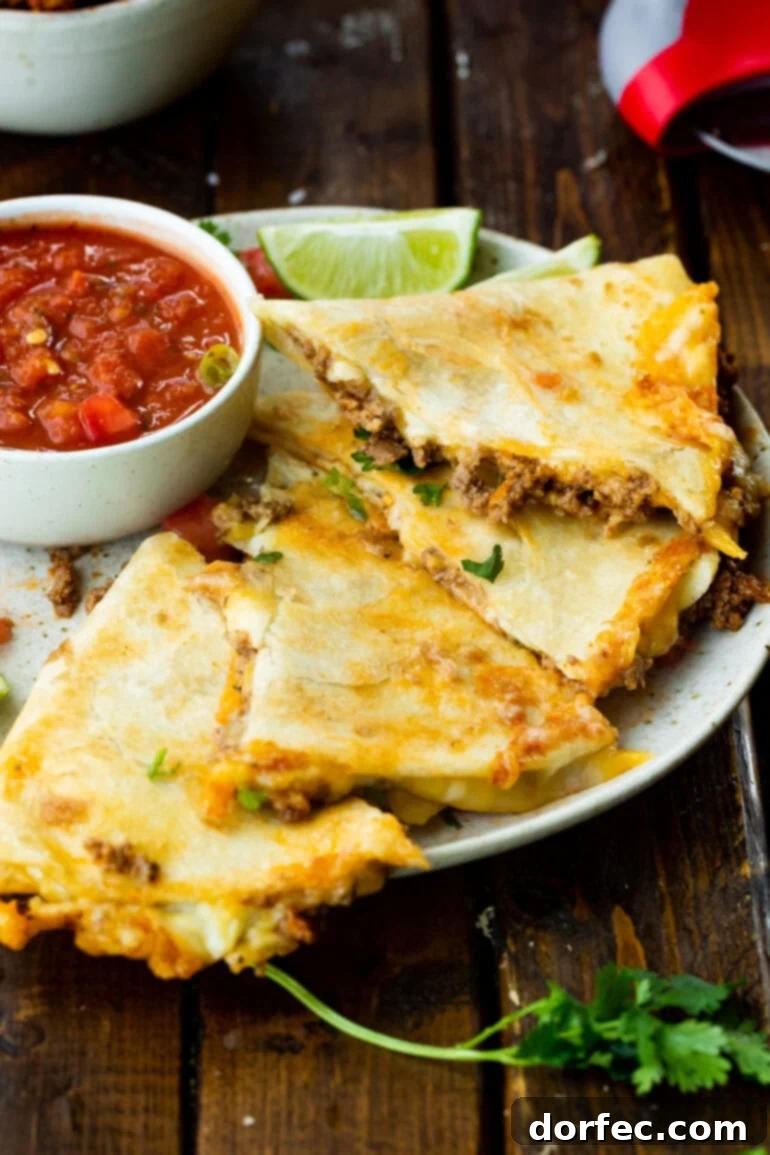 Several triangular segments of golden, cheesy ground beef quesadilla resting on a plate beside a small bowl of vibrant salsa.