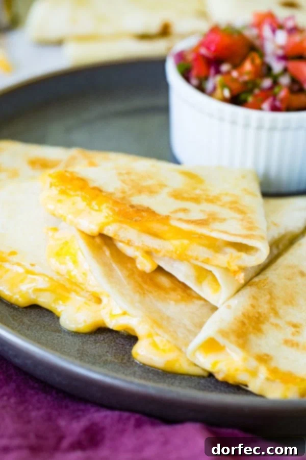 The best quesadilla, perfectly sliced and stacked, with irresistible cheesy filling oozing out, accompanied by a bowl of fresh pico de gallo in the background.