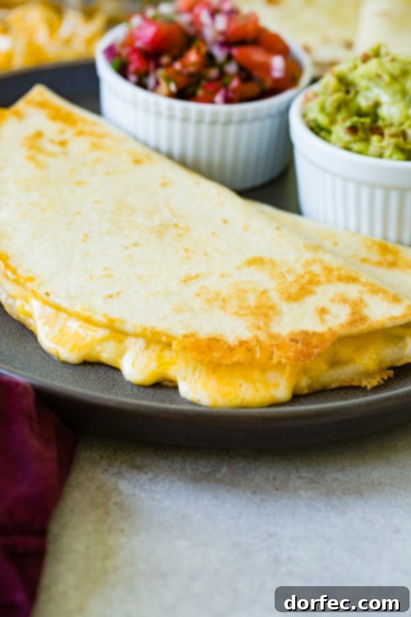 A golden cheese quesadilla presented on a plate, with bowls of fresh pico de gallo and rich guacamole in the background, completing a perfect meal.