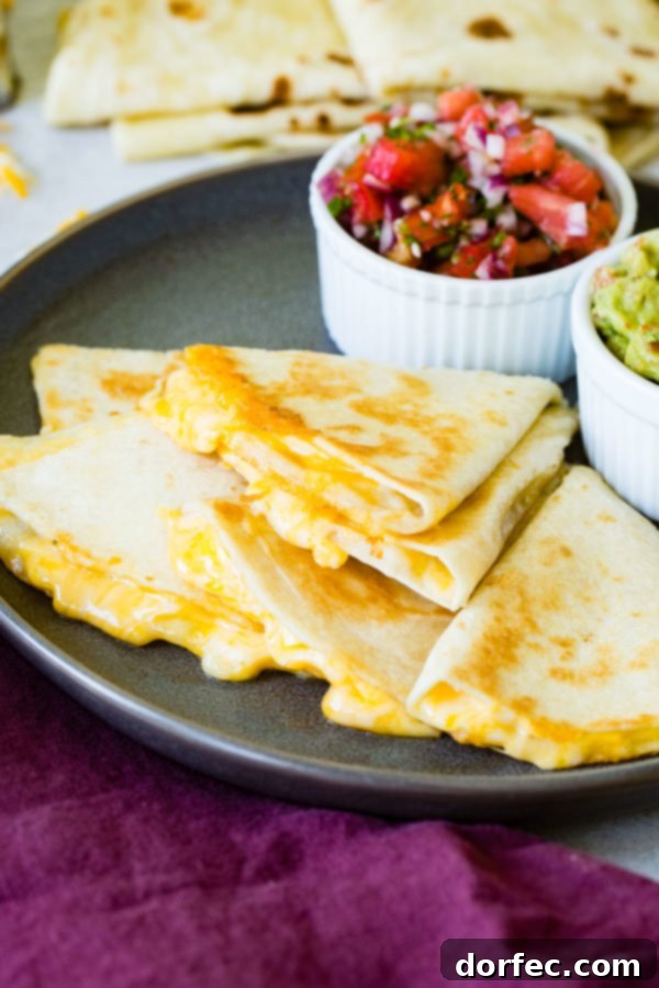 The ultimate quesadilla, sliced and beautifully stacked, showcasing its cheesy interior and accompanied by fresh pico de gallo and creamy guacamole.