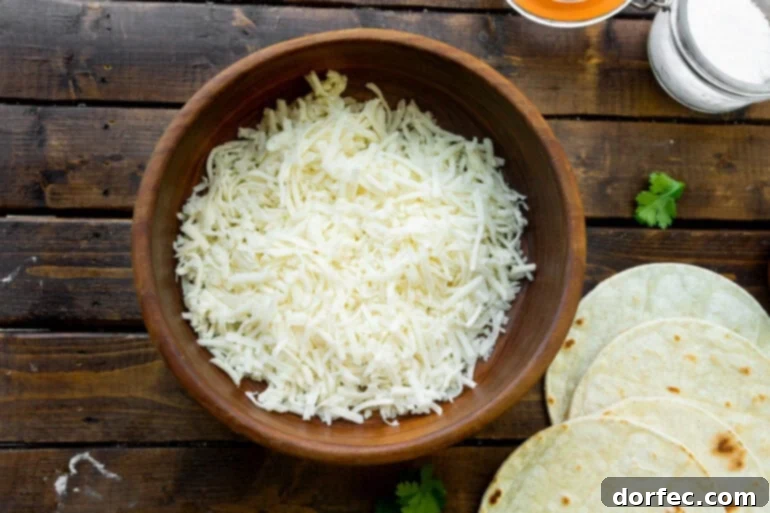 A large wooden bowl filled with freshly grated white Chihuahua cheese, ready for quesadilla making.