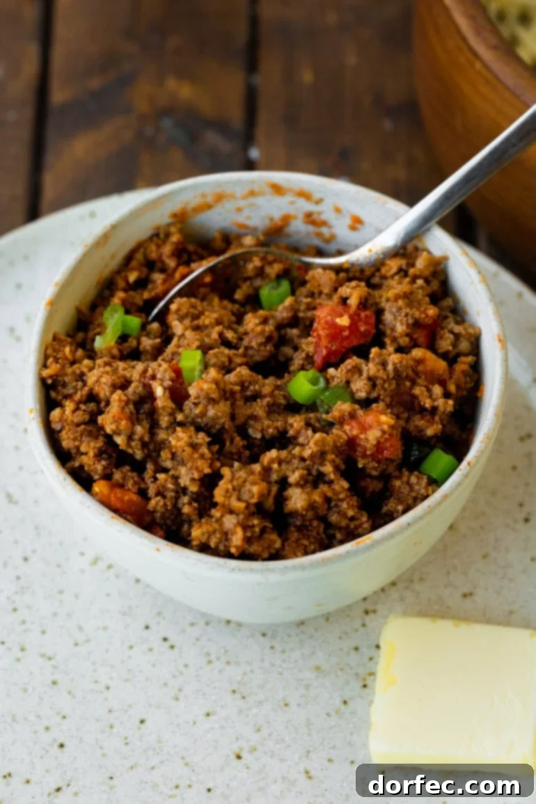 A bowl of savory ground beef, richly cooked with diced tomatoes and vibrant green onions, ready to fill a quesadilla.