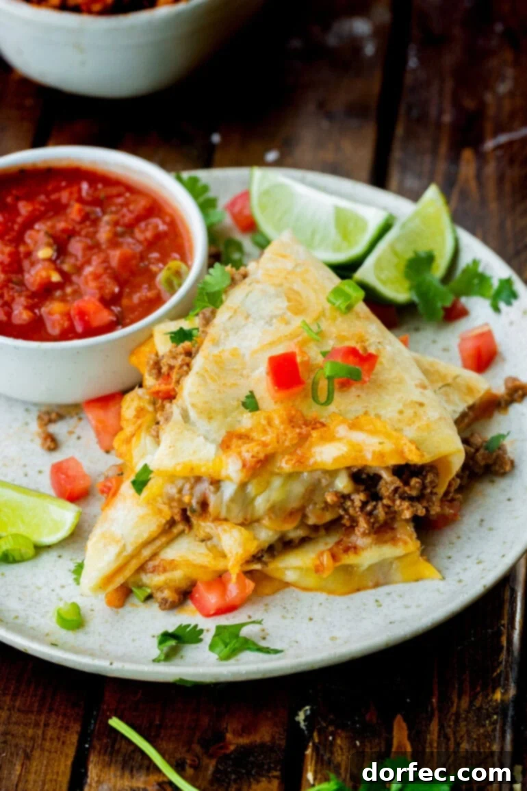 A stack of cheesy ground beef quesadilla pieces next to a small bowl of fresh salsa.
