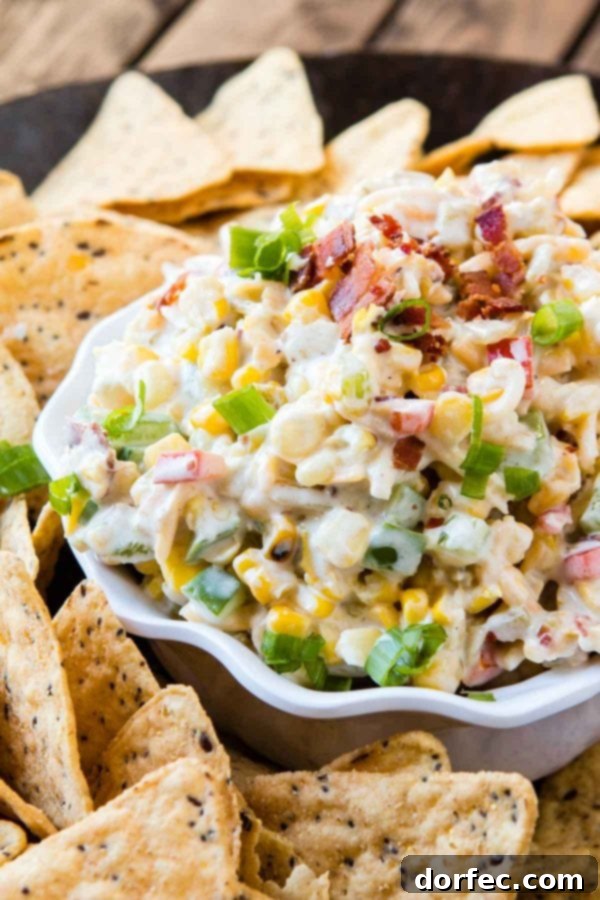 Loaded Cheesy Bacon Ranch Corn Dip 3 Close-up of creamy corn and bacon ranch dip in a white serving dish with a side of tortilla chips, showcasing the rich texture and colorful ingredients.