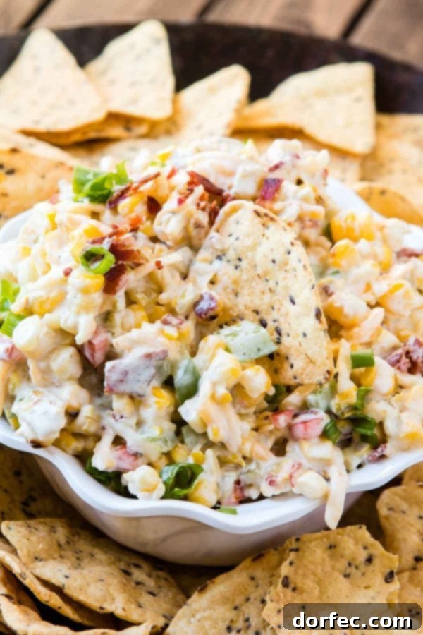 Loaded Cheesy Bacon Ranch Corn Dip 4 A large white bowl brimming with cheesy corn dip, elegantly presented with a scattering of tortilla chips around it, ready to be enjoyed.