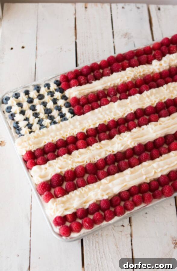 Close-up of a festive Flag Cake, showcasing its fluffy white cake, fresh blueberries, vibrant raspberries, and delicate white buttercream piping, ideal for summer gatherings.