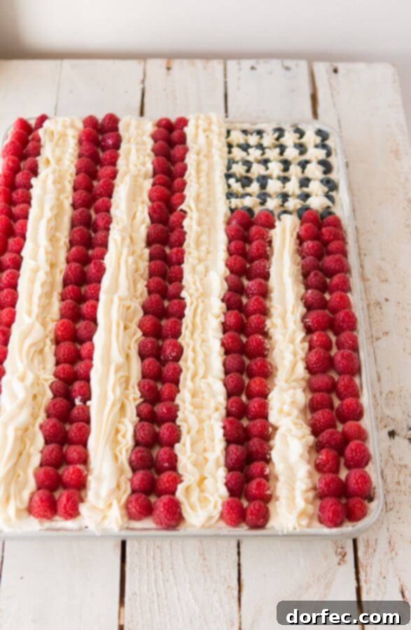 A beautifully decorated Flag Cake featuring a creamy, light whipped cream base, generously topped with fresh blueberries and raspberries, and finished with elegant buttercream stripes.