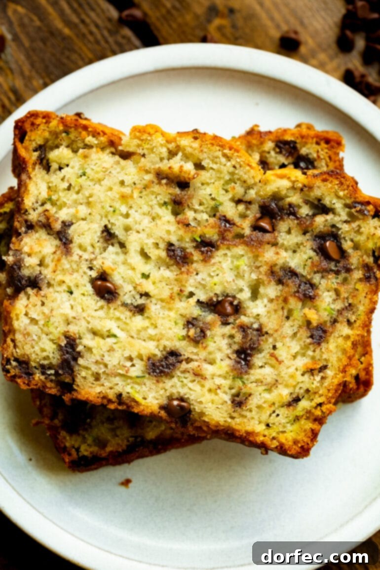 Two slices of moist chocolate chip banana zucchini bread stacked on a white dessert plate, ready to be enjoyed.