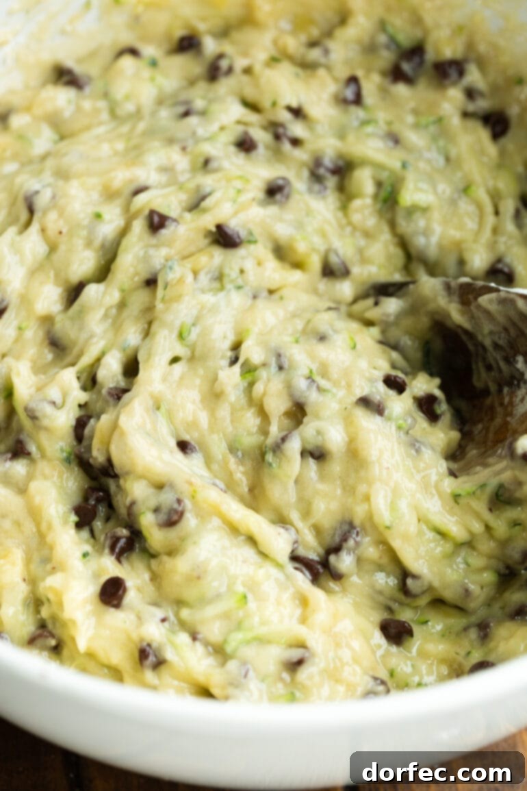 A wooden spoon stirring chocolate chip zucchini banana bread batter in a mixing bowl, showcasing the consistency and ingredients.