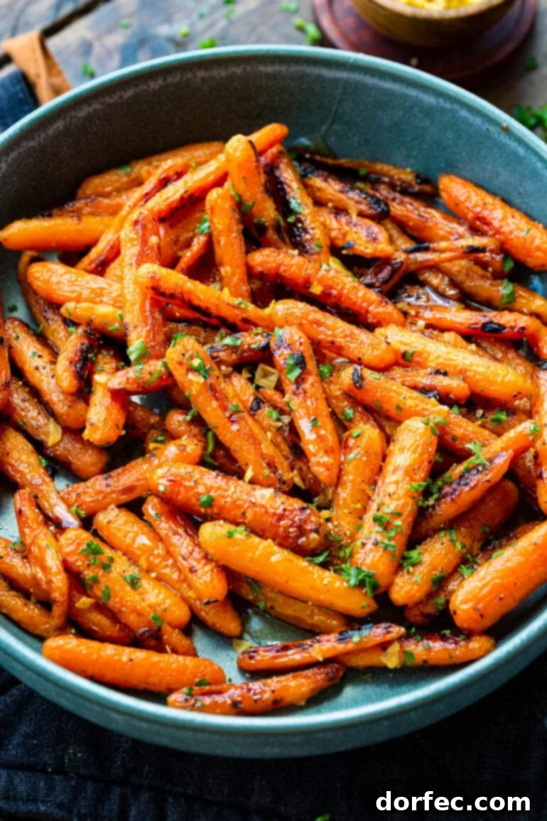 A large blue serving bowl overflowing with golden honey garlic roasted baby carrots, beautifully garnished with chopped fresh herbs.