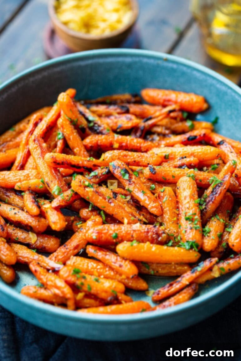 A large blue serving bowl brimming with savory-sweet honey garlic roasted baby carrots, beautifully topped with chopped fresh herbs.