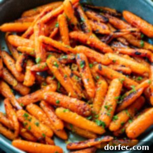 A large blue serving bowl overflowing with golden honey garlic roasted baby carrots, beautifully garnished with chopped fresh herbs.