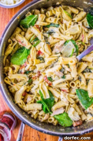 Pesto Chicken Pasta with Sun-Dried Tomatoes and Artichokes Close-up of Pesto Chicken Pasta Garnished with Parmesan