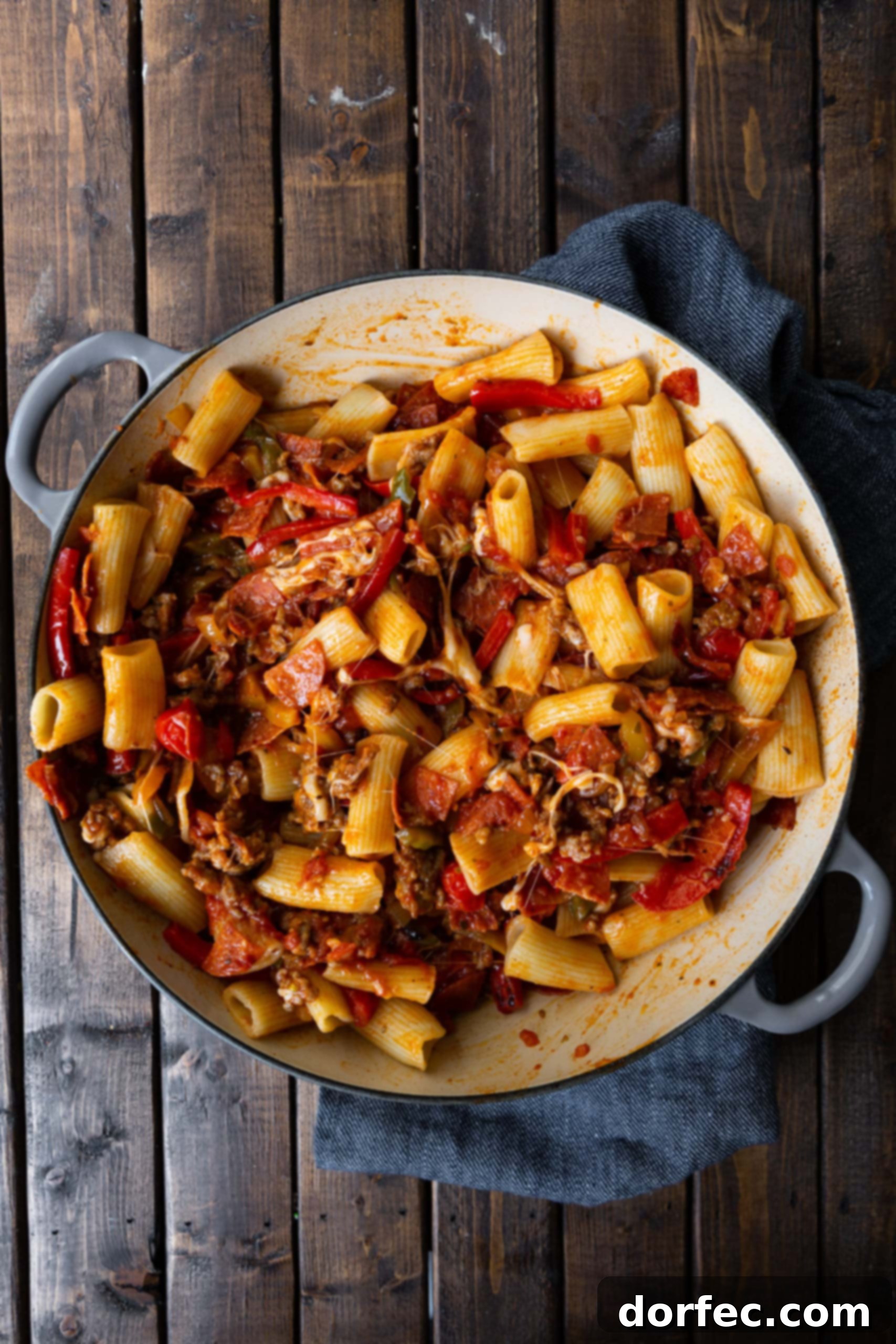 A photo of cooked rigatoni mixed with caramelized peppers and onions, chopped pepperoni and browned Italian sausage. If you love the robust flavors of pizza, then you'll absolutely adore this easy Italian sausage and peppers rigatoni pasta recipe for a comforting family meal.